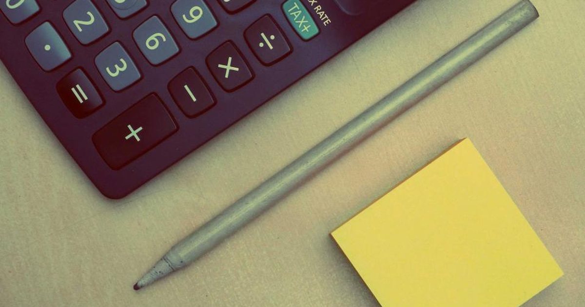 Calculadora con un lápiz y una nota adhesiva amarilla sobre fondo verde
