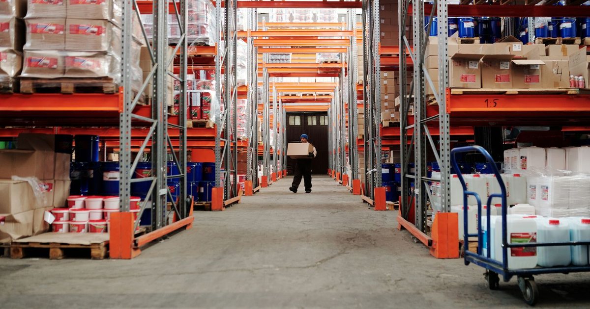 Operario transportando una caja por el pasillo de un almacén industrial