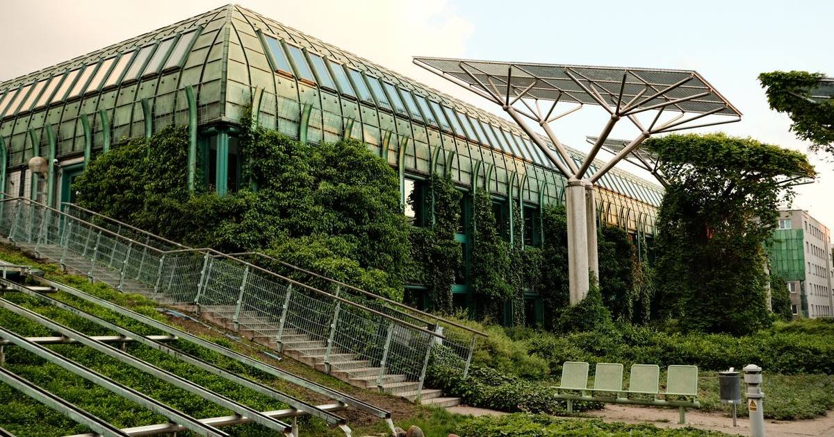 Edificio con fachada acristalada cubierta de vegetación y una marquesina con paneles solares