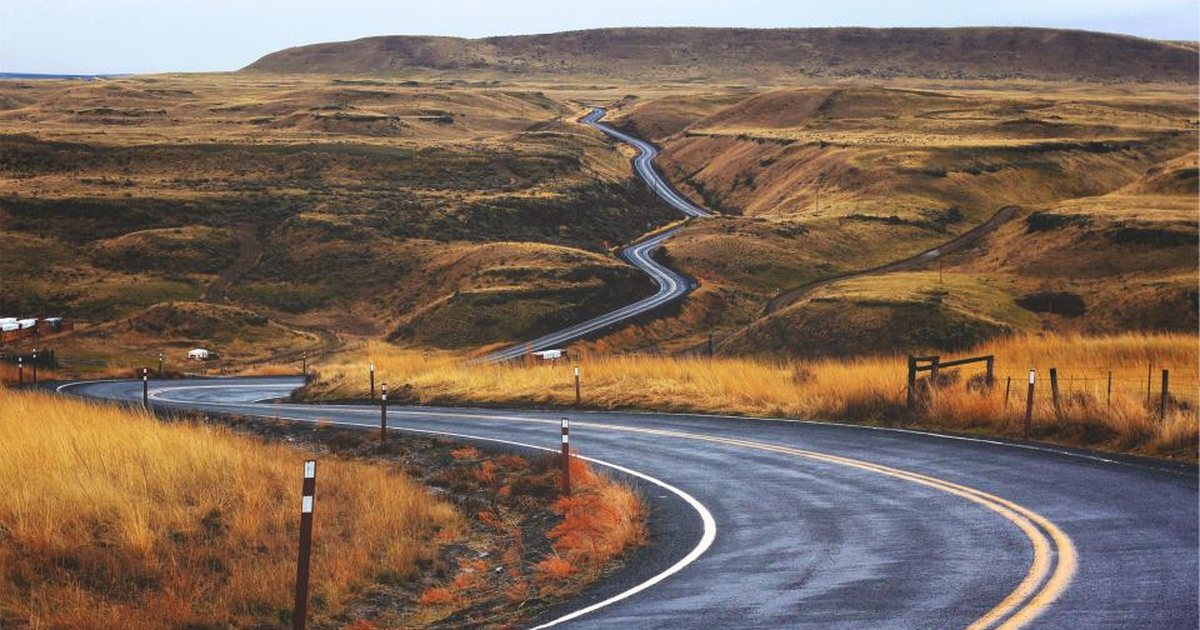 Carretera sinuosa atravesando colinas onduladas de tonos dorados