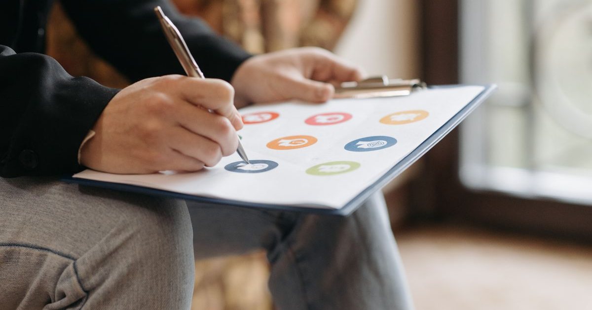Persona rellenando a mano un cuestionario con iconos de colores en una carpeta portapapeles