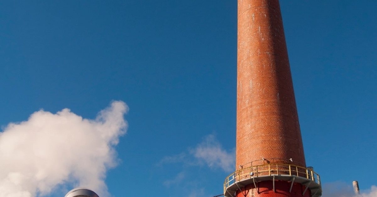 Chimenea industrial alta con tuberías contra un cielo azul despejado