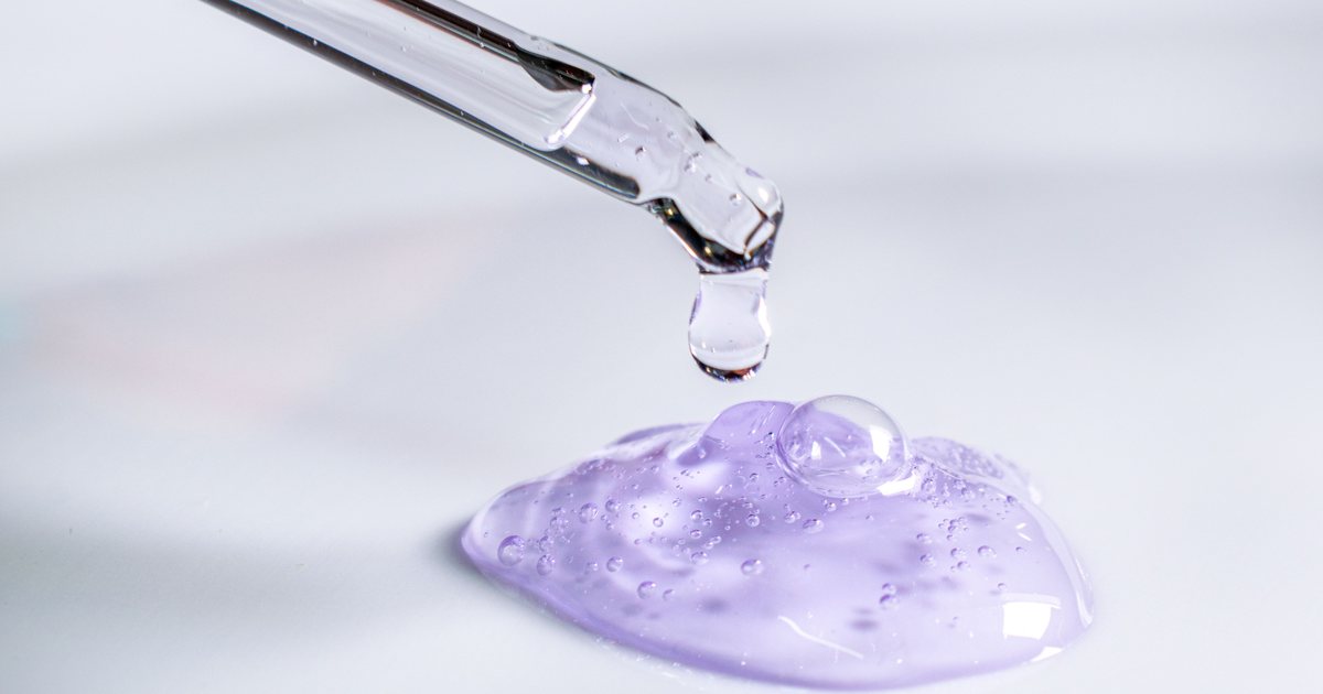 Pipeta de laboratorio dejando caer una gota sobre un gel cosmético de color lila