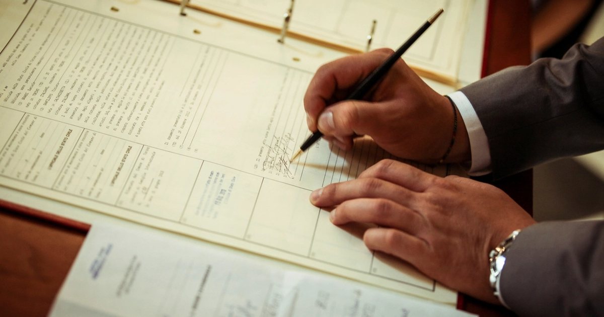 Mano firmando un documento con bolígrafo sobre una mesa de oficina