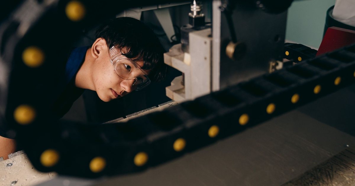 Técnico con gafas de protección inspeccionando de cerca una máquina industrial