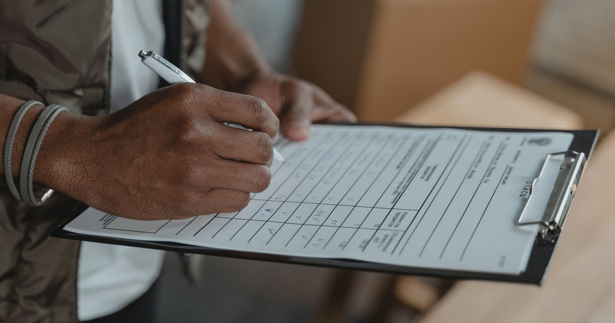 Mano rellenando un formulario de inventario sobre una tablilla con sujetapapeles