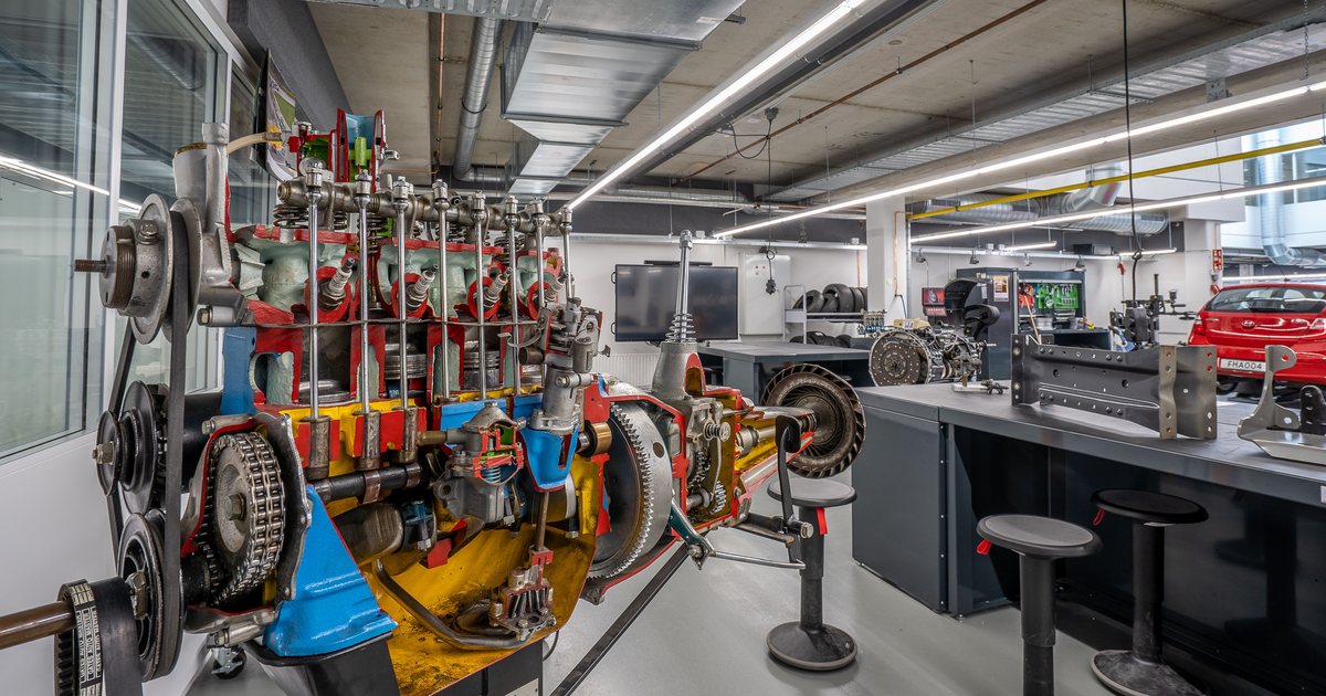 Motor de coche seccionado en un taller técnico de automoción, con herramientas y un vehículo al fondo