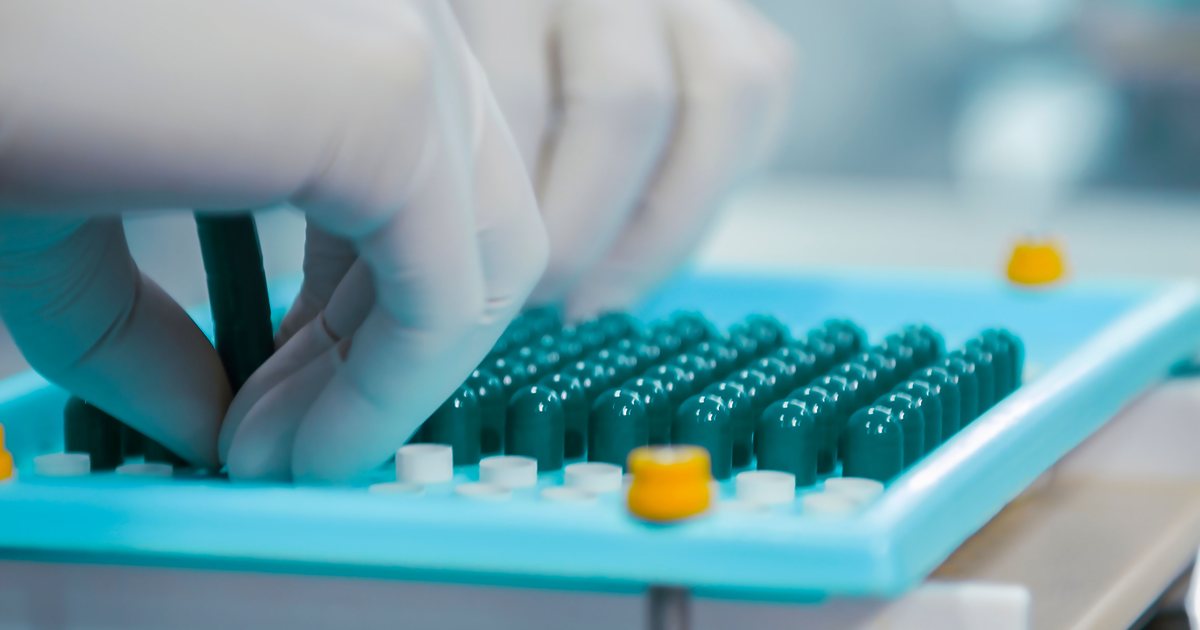 Manos con guantes de látex manipulando cápsulas verdes en una línea de producción farmacéutica