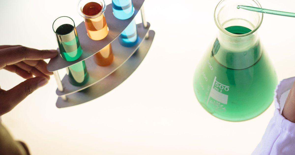 Técnico de laboratorio sujetando un soporte con tubos de ensayo de colores junto a un matraz