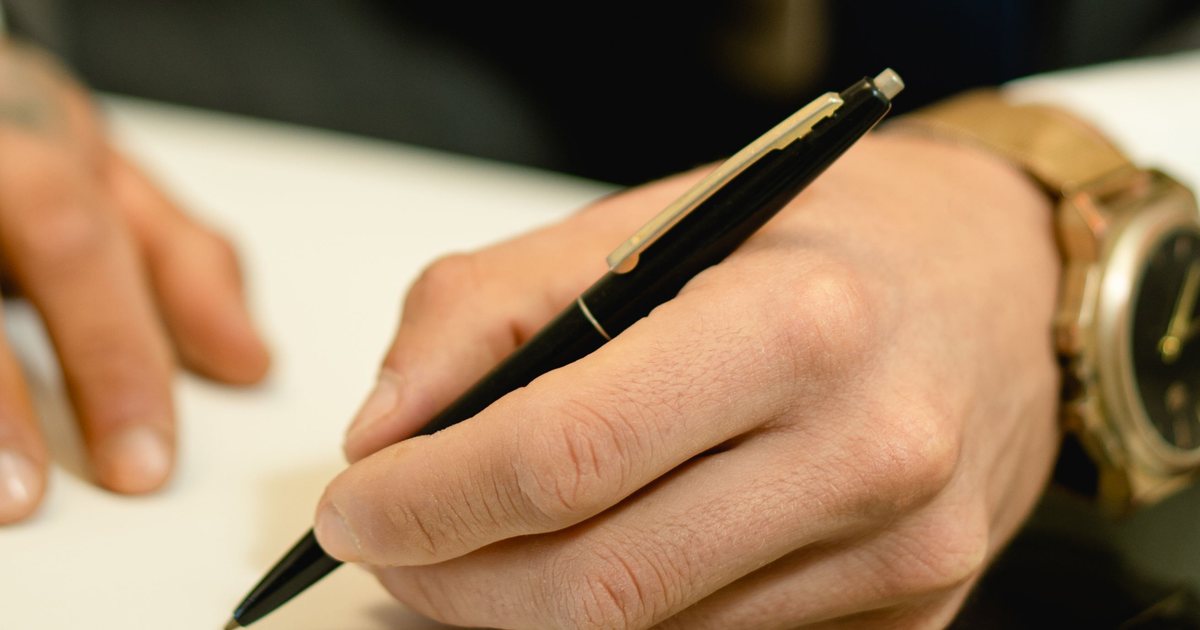 Primer plano de una mano firmando un documento con bolígrafo
