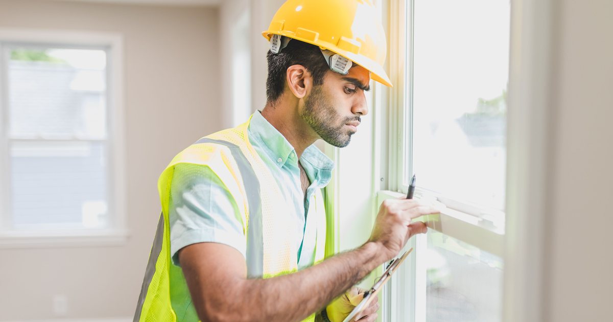 Trabajador con casco y chaleco de seguridad revisando una ventana en una obra