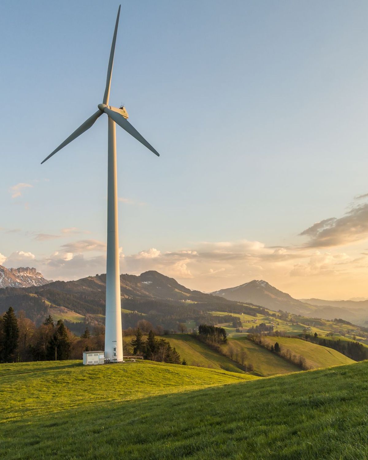 Aerogenerador sobre una ladera verde con montañas y luz de atardecer