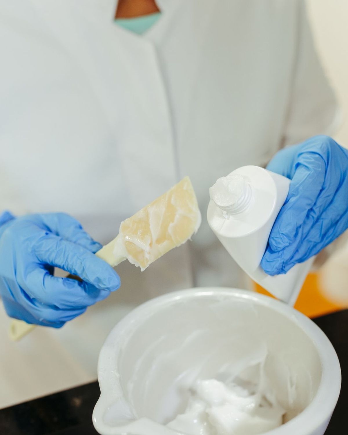 Manos con guantes azules elaborando una crema cosmética en un cuenco