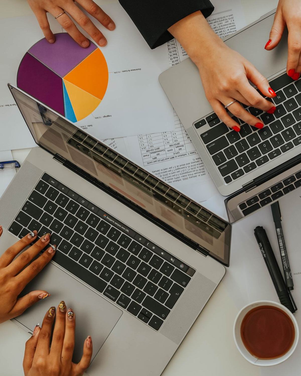 Manos sobre portátiles y gráficos de colores en una mesa de trabajo, vista cenital